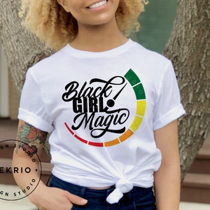 Pu&ograve; includere: Maglietta bianca con una grafica nera che dice "Black Girl Magic" con un cerchio colorato intorno al testo.