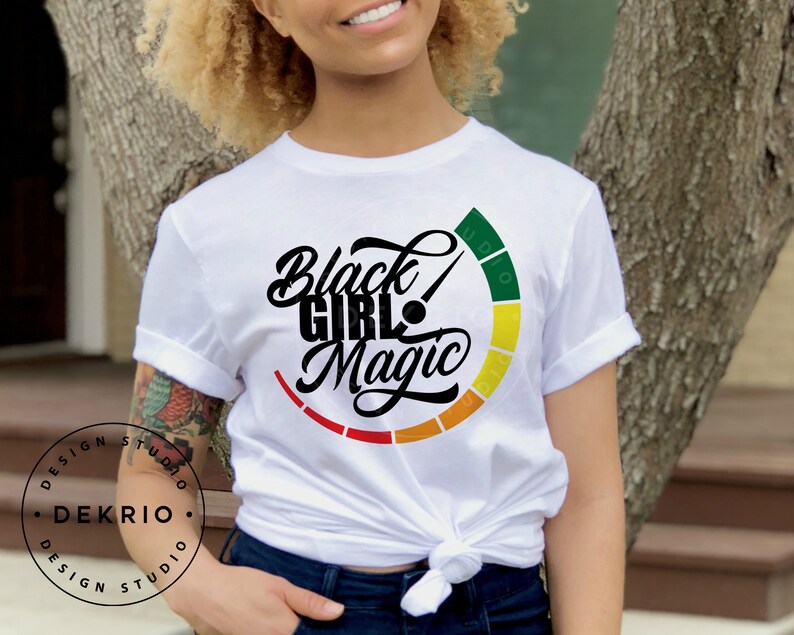 Pu&ograve; includere: Maglietta bianca con una grafica nera che dice "Black Girl Magic" con un cerchio colorato intorno al testo.