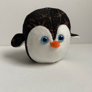 May include: A black and white plush penguin with orange beak and blue eyes. The penguin has a sparkly black and orange pattern on its back.