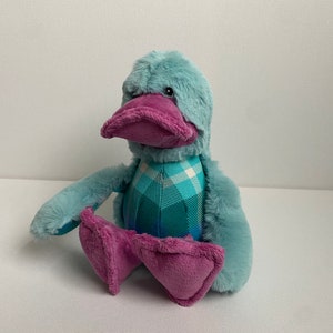 May include: A plush duck toy with a blue and green plaid pattern and a purple beak and feet.