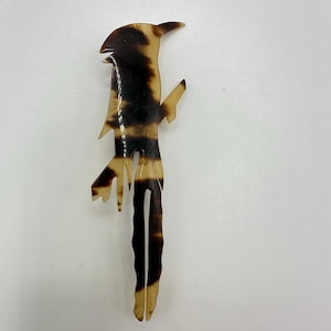 Könnte beinhalten: Dekoratives Haaraccessoire in Form eines Vogels. Die Haarspange besteht aus hellbraunem und dunkelbraunem Material. Der Vogel sitzt auf einem Ast. Die Haarspange ist etwa 15 cm lang.