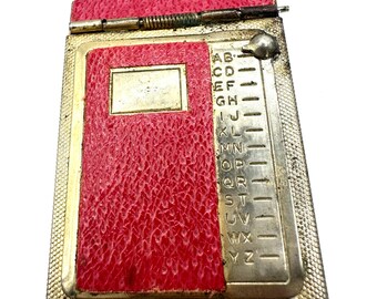 Bloco de notas compacto vintage em latão vermelho com mecanismo deslizante para contatos telefônicos e endereços.