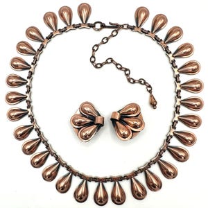 May include: A copper-toned jewelry set featuring a necklace and matching earrings. The necklace has a series of teardrop-shaped pendants. The earrings are composed of a cluster of teardrop shapes. The set is displayed on a white background.