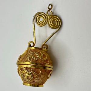 May include: A gold-toned tea infuser with a mesh basket and decorative floral cutouts. The handle features a heart-shaped design with spiral accents. The infuser is designed to open and close for easy filling and cleaning.