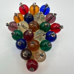 Puede incluir: Un grupo de cuentas de vidrio redondas y coloridas en varios colores, incluyendo rojo, naranja, azul y verde. Cada cuenta tiene un pequeño lazo de metal en la parte superior. Las cuentas están dispuestas juntas, creando una exhibición visualmente atractiva.