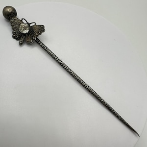 May include: Silver hair stick with a butterfly design and a clear rhinestone. The stick has a textured surface.