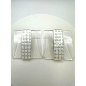 May include: A pair of rectangular clear glass clips featuring a central vertical band with a white polka dot pattern. Each piece has a smooth, transparent outer section and a textured, opaque white center strip with a repeating circular design.