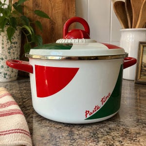 Puede incluir: Una olla de esmalte blanco con detalles geométricos rojos y verdes y una tapa a juego. La olla cuenta con dos asas laterales rojas y un pomo rojo en la tapa. El texto "Pasta time" está impreso en color rojo en el cuerpo de la olla.