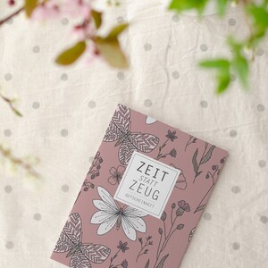 May include: A pink booklet with a floral and butterfly design. The text on the cover reads "Zeit statt Zeug Gutscheinheft".