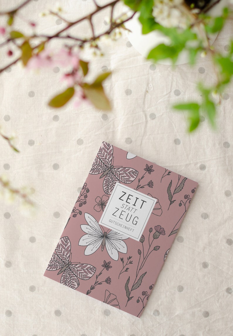 May include: A pink booklet with a floral and butterfly design. The text on the cover reads "Zeit statt Zeug Gutscheinheft".
