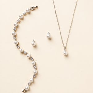 A delicate necklace, bracelet, and earrings are arranged on a light-colored background.