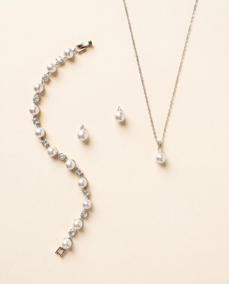 A delicate necklace, bracelet, and earrings are arranged on a light-colored background.