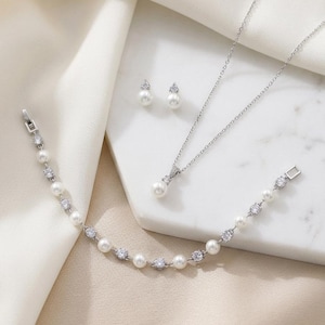 A delicate necklace, bracelet, and earrings are arranged on a white marble surface, creating an elegant and sophisticated display.