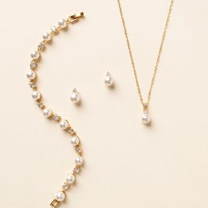 A delicate gold necklace, earrings, and bracelet are arranged on a light-colored background.