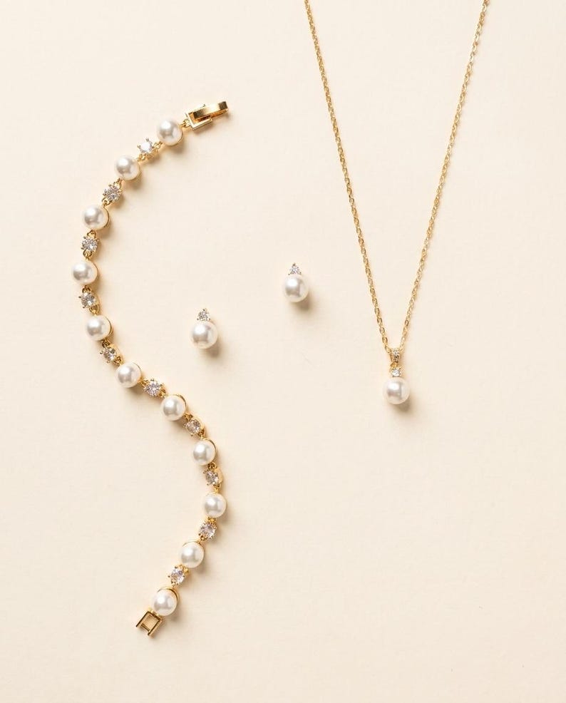 A delicate gold necklace, earrings, and bracelet are arranged on a light-colored background.