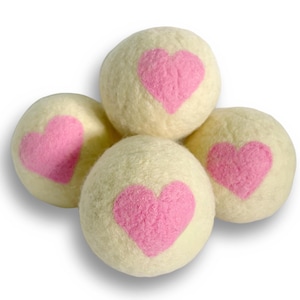 May include: Four cream-colored felt balls with pink heart designs. The balls are arranged in a cluster, with each ball featuring a prominent pink heart. The felt balls are a soft, textured material.
