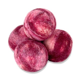 May include: Four felted wool balls in shades of pink and burgundy are stacked together. The balls have a textured, marbled appearance, with lighter pink swirls throughout the darker hues. The balls are arranged against a white background.