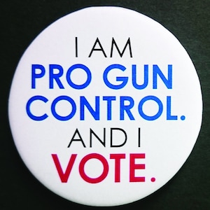May include: A white button with the text "I AM PRO GUN CONTROL. AND I VOTE." in black, blue, and red lettering.