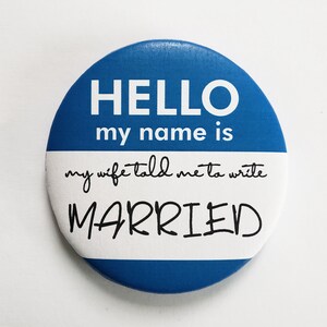May include: Blue and white round button with the text "HELLO my name is my wife told me to write MARRIED".