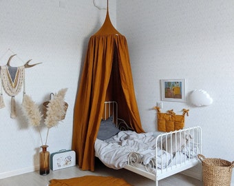 May include: A child's bedroom with a white metal bed, a mustard-colored canopy, and a leaf-shaped rug. The room is decorated with a small suitcase, a woven basket, and a wall hanging. The walls are white.