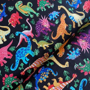 May include: Black fabric featuring a colorful dinosaur pattern. The dinosaurs are depicted in various colors, including red, green, blue, and yellow, with a variety of shapes and sizes. The fabric also includes green plant illustrations.