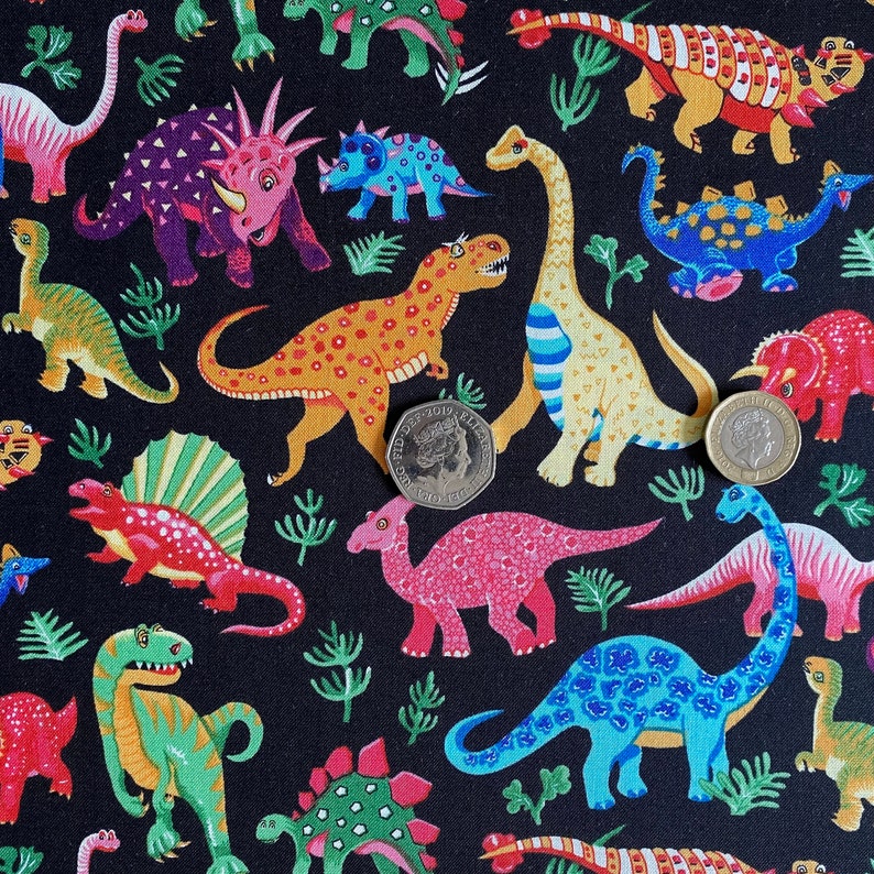 May include: A black fabric featuring a colorful dinosaur pattern. The dinosaurs are in various colors, including red, green, yellow, and blue, with a variety of patterns. The design includes stylized plant life and two coins.