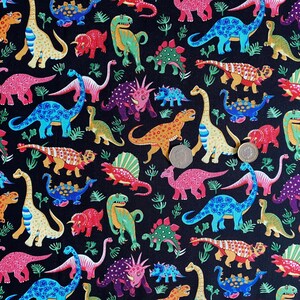 May include: A black fabric featuring a colorful dinosaur pattern. The dinosaurs are in various colors, including blue, pink, green, and orange, with some having spots and stripes. The design includes ferns and various dinosaur species.