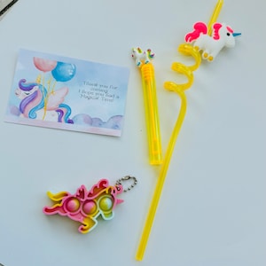 Peut inclure: Un ensemble de cadeaux de fête sur le thème de la licorne avec une paille jaune surmontée d'une licorne, un porte-clés licorne avec un jouet à bulles et une carte de remerciement qui dit "Merci d'être venu. J'espère que vous avez passé un moment magique !"