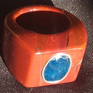 May include: A red, orange, and black ring with a blue stone set in silver. The ring is made of a natural stone and has a unique, organic look.