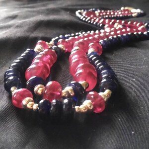 May include: A multi-strand necklace with pink and blue beads. The necklace is made of glass beads and has a gold metal clasp.
