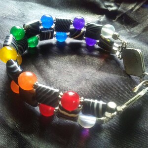 Könnte beinhalten: Ein Armband mit Regenbogenfarben, schwarzen und weißen Perlen und einem silbernen Verschluss.