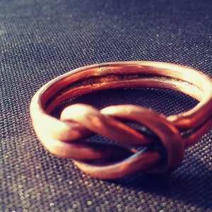 May include: A copper ring with a knot design. The ring is made from a single piece of wire that is twisted and knotted together.