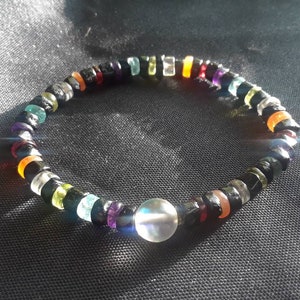 Puede incluir: Un brazalete de cuentas de colores con un dije de cristal transparente. El brazalete tiene cuentas negras, naranjas, rojas, verdes, azules y moradas.