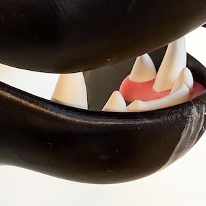 May include: Close-up of a black and white animal mask with a set of white teeth and a pink tongue.