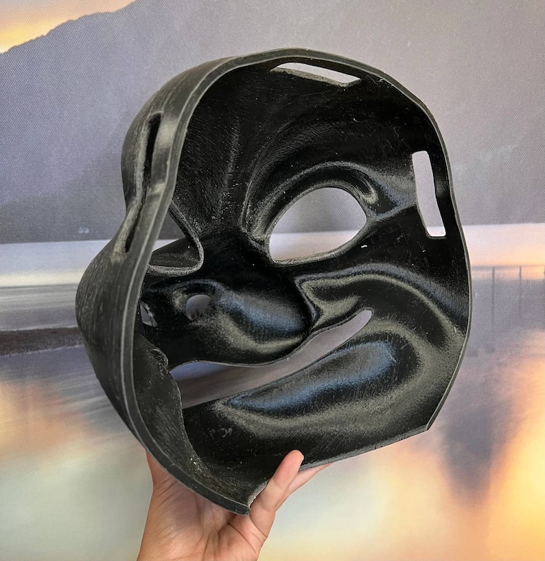 Puede incluir: M&aacute;scara de pl&aacute;stico negro con una superficie texturizada y aberturas para los ojos y la boca. La m&aacute;scara est&aacute; dise&ntilde;ada para parecerse a un rostro humano.