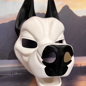 May include: A white and black dog mask with large, pointed ears. The mask features a detailed snout and eye openings. The ears and nose are black, contrasting with the white face. The mask is likely for cosplay or costume use.