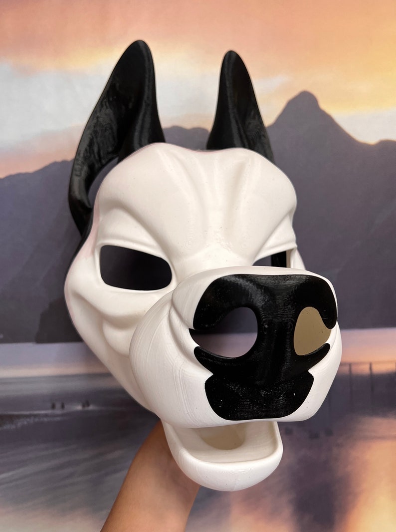 May include: A white and black dog mask with large, pointed ears. The mask features a detailed snout and eye openings. The ears and nose are black, contrasting with the white face. The mask is likely for cosplay or costume use.