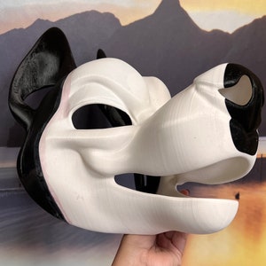 May include: A white and black dog mask with a 3D printed appearance. The mask features a dog snout, ears, and eye openings. The ears and parts of the snout are black, while the rest of the mask is white.