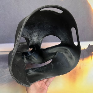 Op de afbeelding: Zwart plastic masker met een getextureerd oppervlak en twee ooggaten. Het masker is ontworpen om de neus en mond te bedekken.