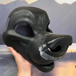 Op de afbeelding: Een zwart bont masker met een gedetailleerde snuit en een getextureerd oppervlak. Het masker is gemaakt van een hard materiaal en heeft een realistische uitstraling.