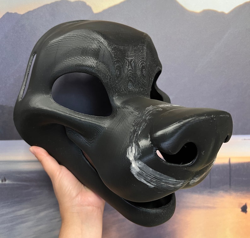 Op de afbeelding: Een zwart bont masker met een gedetailleerde snuit en een getextureerd oppervlak. Het masker is gemaakt van een hard materiaal en heeft een realistische uitstraling.