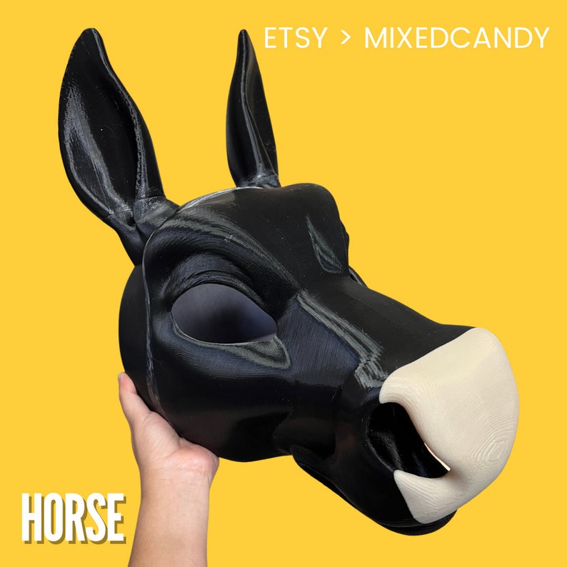 May include: Black horse head mask with a white nose. The mask is made of a smooth, hard material and has a realistic look. The mask is being held by a hand.