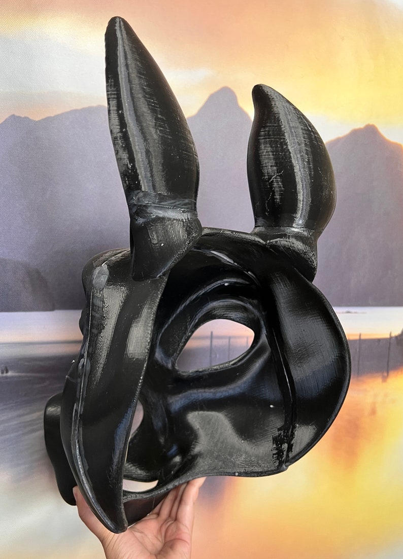 May include: A black, 3D printed mask with long, pointed ears. The mask has a smooth, glossy finish and is designed to cover the eyes and nose.