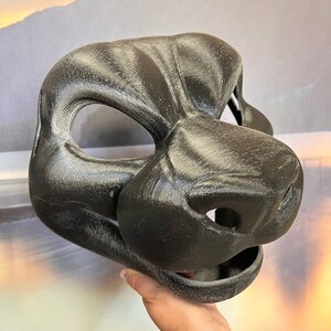 Puede incluir: Una m&aacute;scara de animal de piel negra con un hocico detallado y ojos grandes. La m&aacute;scara est&aacute; hecha de un material liso y texturizado.