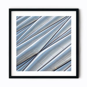 May include: Abstract architectural photograph of a building with a geometric pattern of curved, silver panels. The panels create a wave-like effect, with light reflecting off their surface.