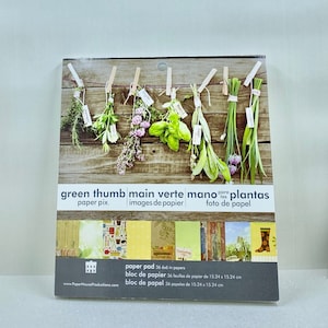 May include: A pack of 36 6x6 inch paper pads with a green thumb theme. The front of the pack features a photo of herbs hanging on a wooden surface. The text on the pack reads "green thumb main verte mano para las plantas paper pix. images de papier foto de papel".