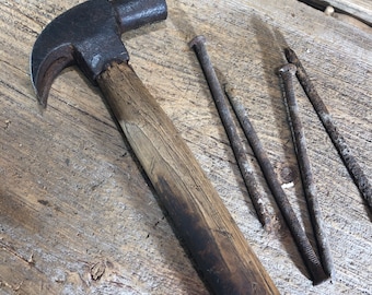 May include: A vintage claw hammer with a wooden handle and four rusty nails on a wooden surface.
