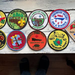 May include: Nine embroidered patches with various designs and text, including "Pinewood Derby", "Greater East Side", "Cuisine-O-Ree", "Webelos Woods", "Indianhead Council", "GES", and "B.S.A.".
