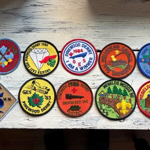 May include: Ten colorful embroidered patches with various designs and text, including "Pinewood Derby", "GES", "I am a Winner", "Webelos Woods", and "Be Prepared".