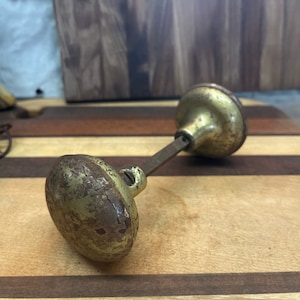 May include: A vintage brass door knob with a worn finish. The knob is attached to a metal rod and has a round shape.
